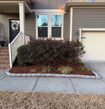 Mulched landscape bed with a low stone border beside a house entrance