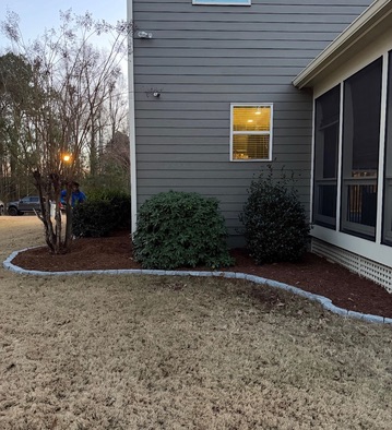 Mulched bed with shrubs and stone edging beside a screened porch