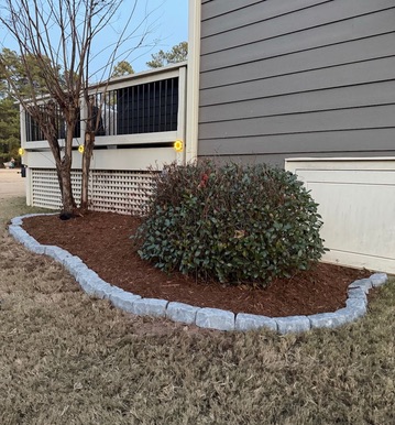 Curved stone edging around a mulched bed with shrubs and a tree