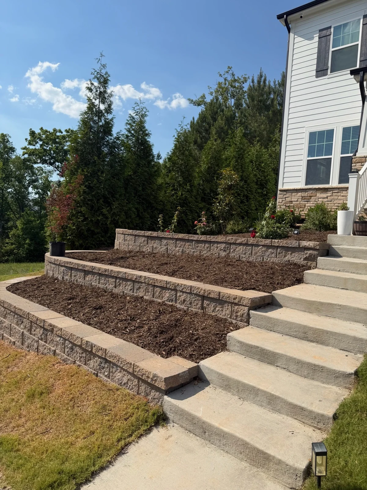 Three levels of block retaining walls beside concrete steps and planted beds. YardU project photo.