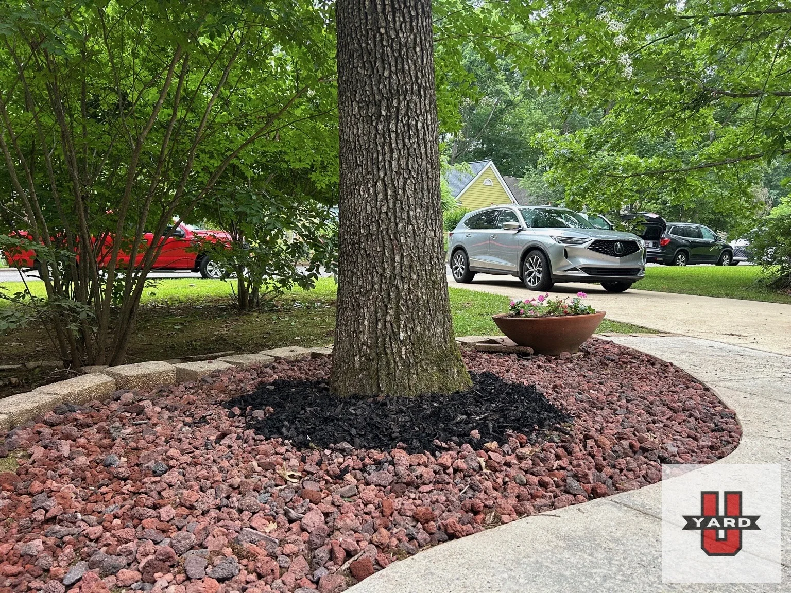 A rounded decorative rock bed frames a mature tree beside the driveway. YardU project photo.